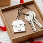 Keychain house and keys with red ribbon and gift box on white wooden background